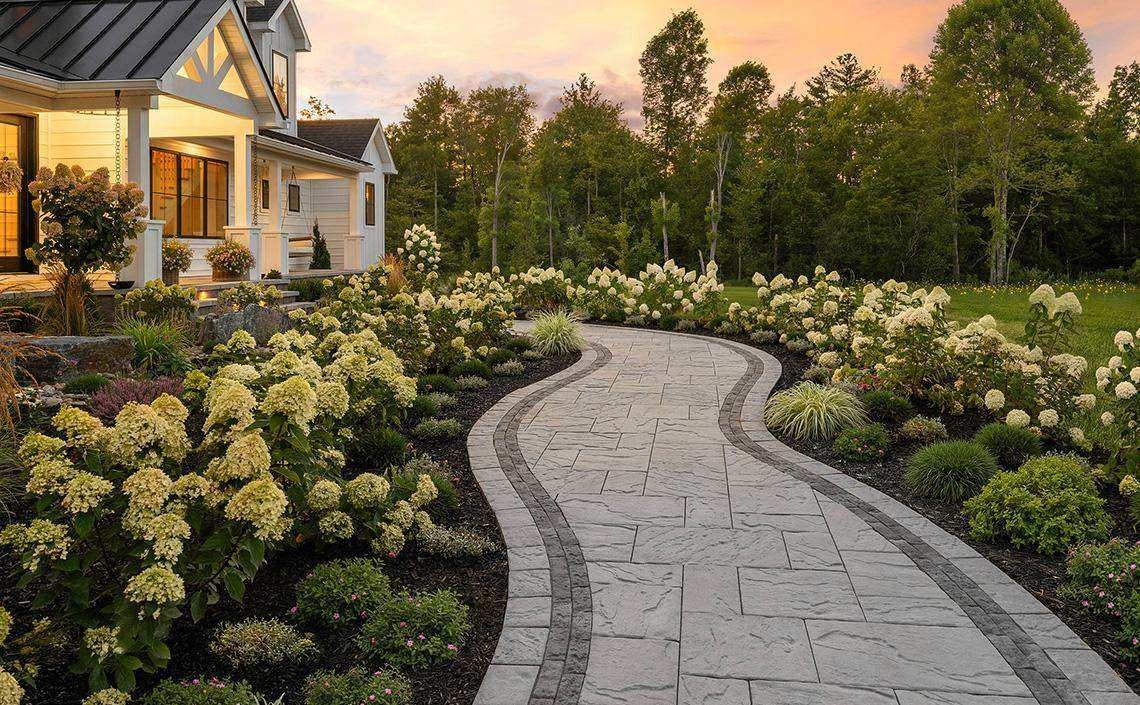 Landscaped front walkway with hydrangeas and perennial beds leading to a New England home