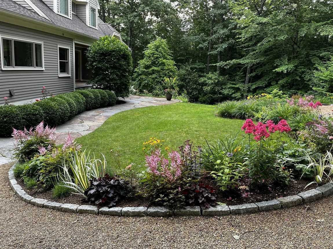 Freshly edged lawn, mulched perennial beds and stone edging maintained by Vcoelho General Services